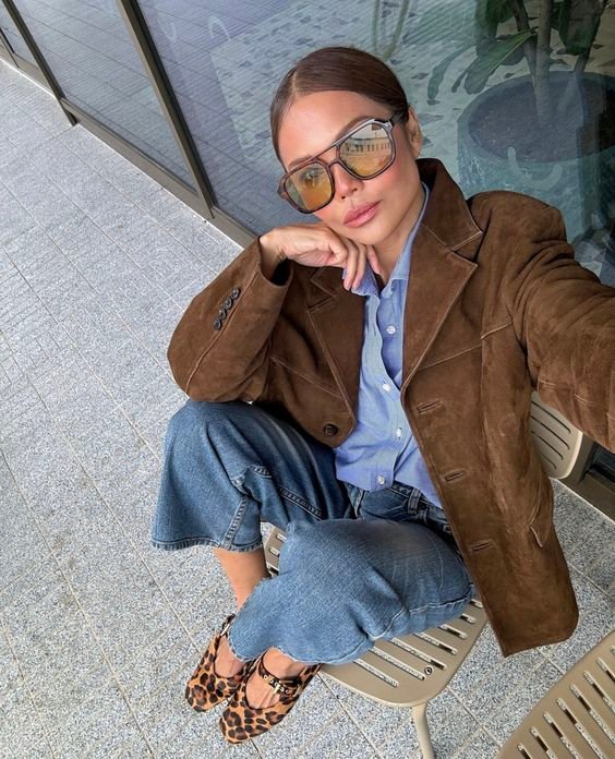 Femme portant lunettes aviateur, chemise bleu clair, jeans clair et ballerines motif léopard